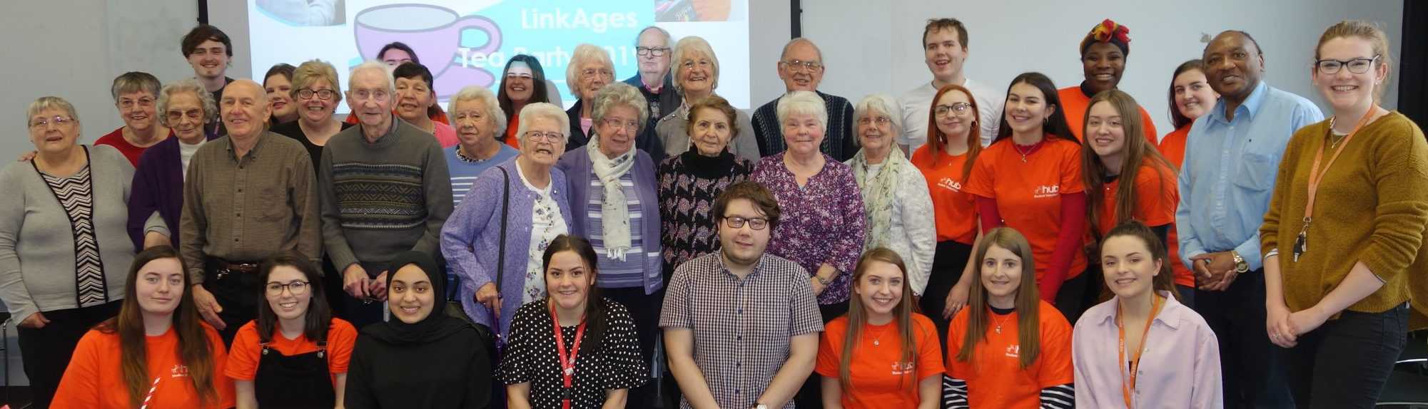 A group of people smile at the camera. The group includes student volunteers and LinkAges community participants.