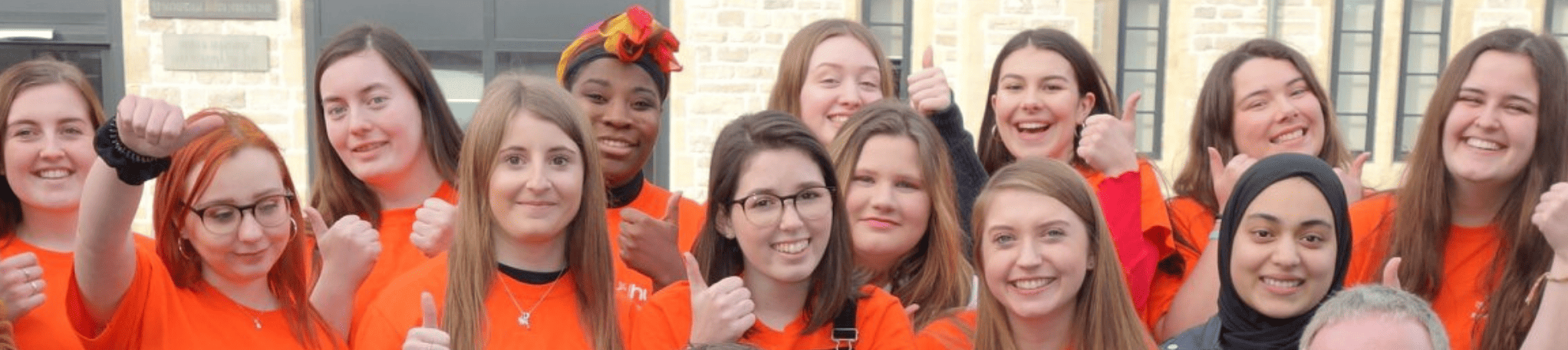 A group of student volunteers wearing orange t-shirts smile at the camera.