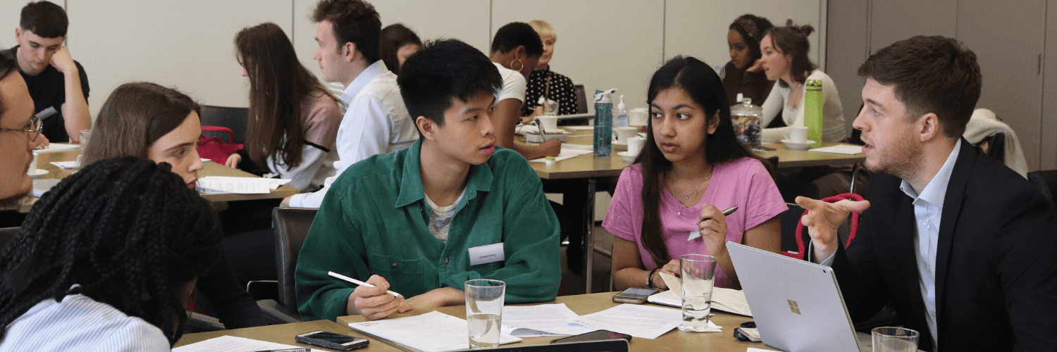 Five people are in discussion around a table. In the background two other groups are visible.