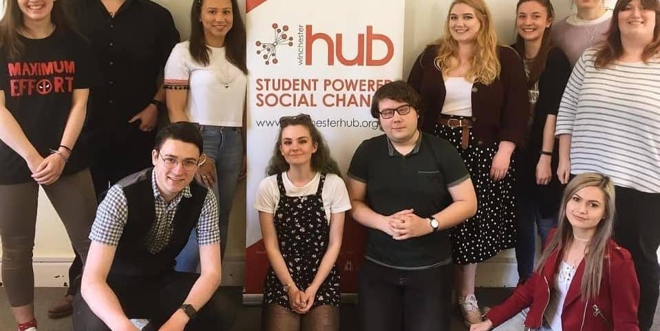 A picture of the Winchester Hub committee from 2019 to 2020. They are posing around a Winchester Hub stand-up banner and smiling at the camera.