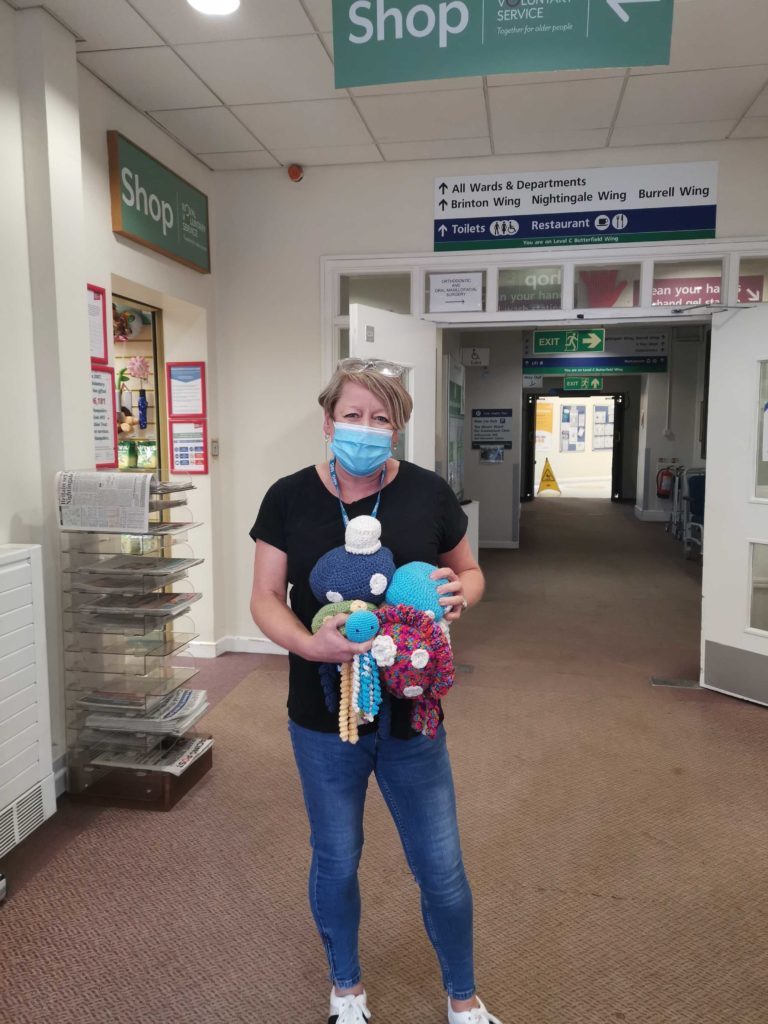 A community partner stands in a hospital corridor holding four colourful knitted octopi 