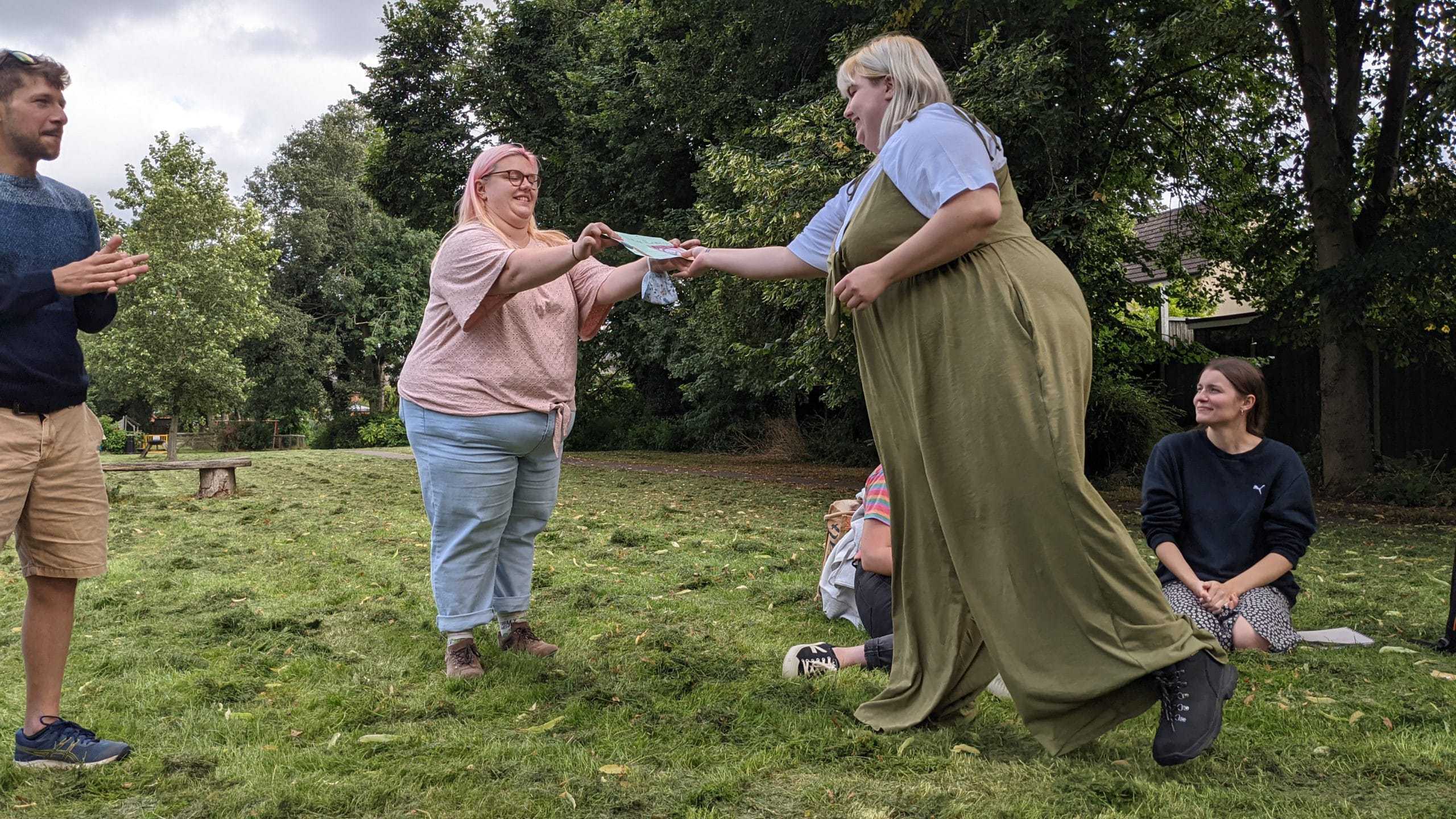 One member of the Student Hubs staff team passes a certificate to another member of the team. You can see three other individuals clapping. 