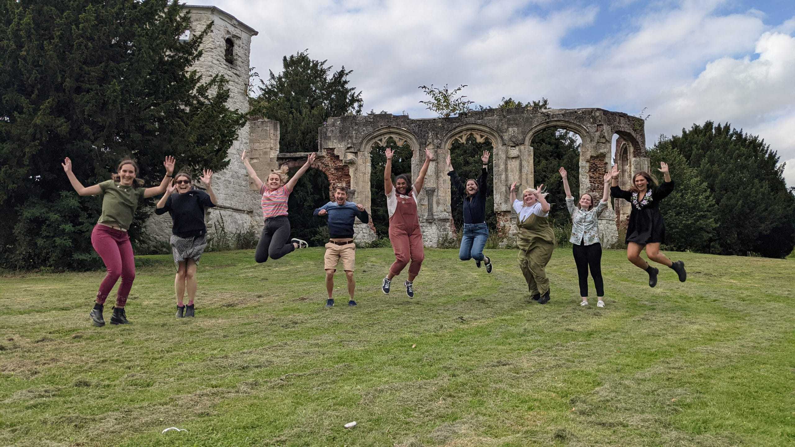 9 members of the Student Hubs staff team jump in front of some ruins in a park.