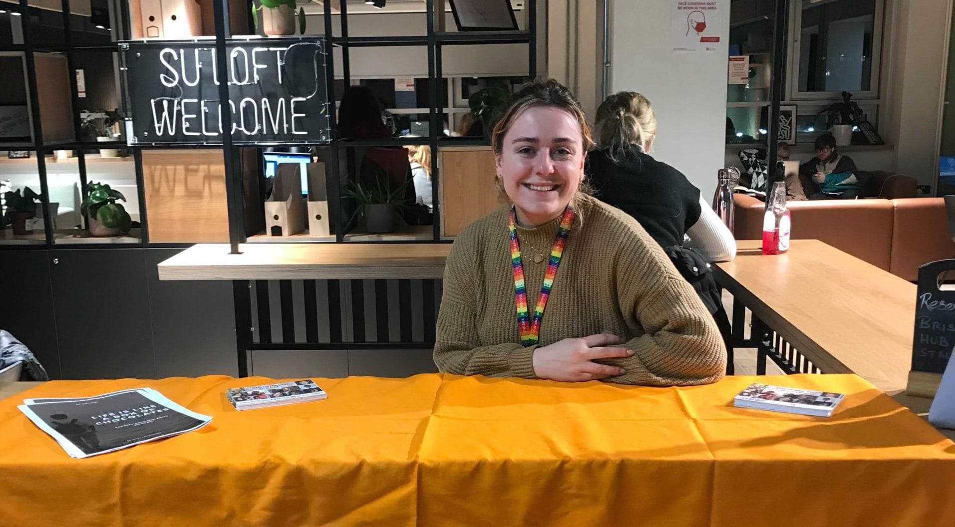 Bristol Hub Programme Manager, Elle, sits down behind a table with an orange tablecloth.