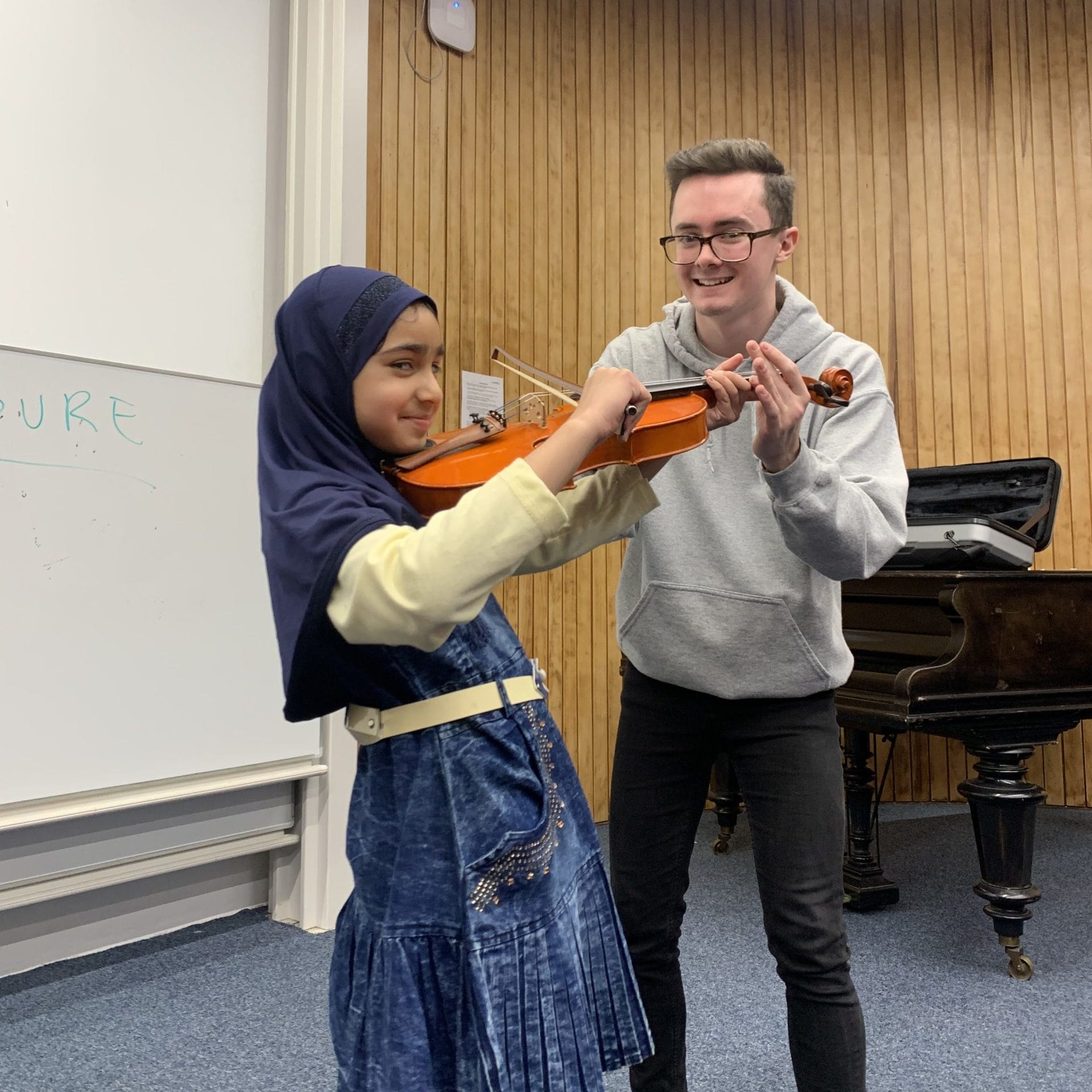 A young person is playing the violin and a student mentor is next to them helping them 