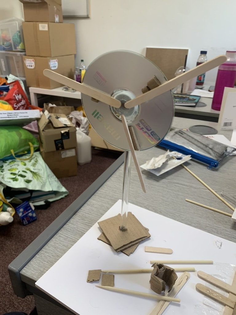 A wind turbine is pictured on a desk made out of a CD and lollipop sticks