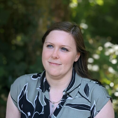 Student Hubs Partnerships and Development Director, Fiona, stands in front of foliage smiling. She is looking slightly to the left.