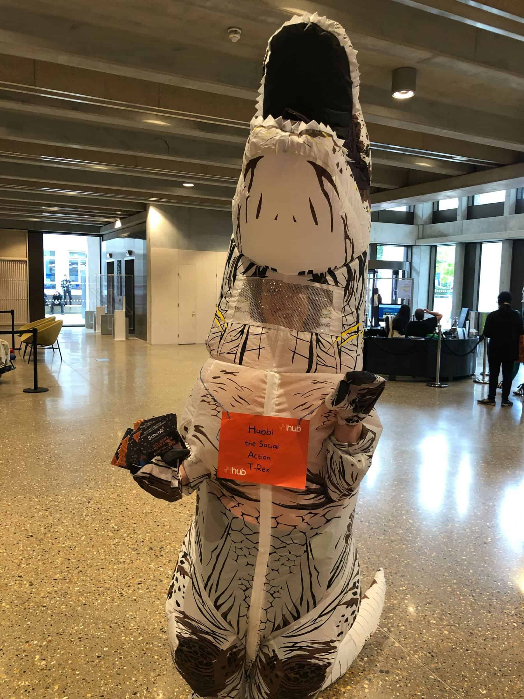 Kingston Hub Staff Member wearing a T-Rex suit with a tag around their neck with the writring 'Hubbi The Social Action T-Rex'
