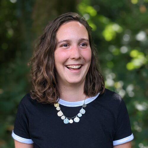 Bristol Hub Manager, Sorcha, stands in front of foliage smiling. She is looking slightly to the left.