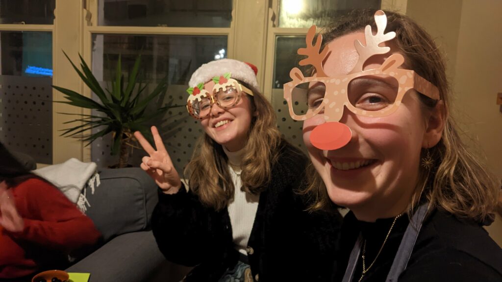 Two staff members looking and smiling at the camera while wearing Christmas glasses one as a Christmas pudding and other as a reindeer.