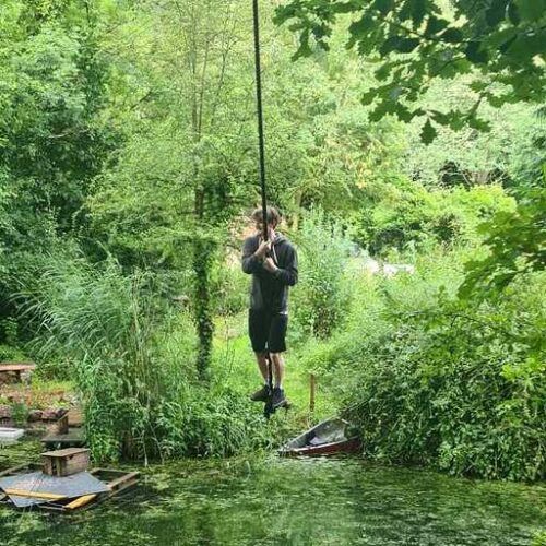 ID: Charlie balances over water in a green, wooded area.