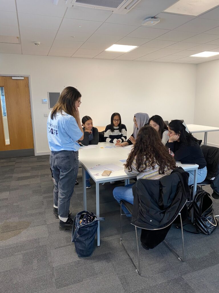 ID: a volunteer chats to a table of students in a classroom