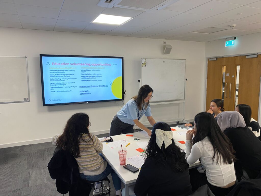 ID: a volunteer chats to a table of students in a classroom