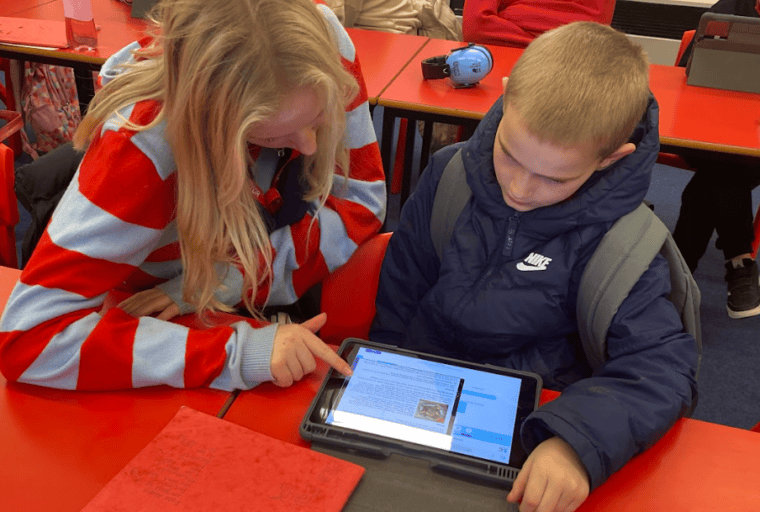 ID: a Bristol Hub volunteer works on an iPad with a young person in a classroom