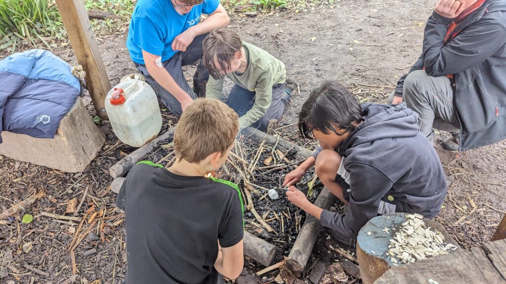 ID: young people crouch over a firepit