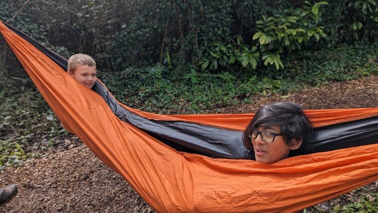 ID: two young people sit in an orange hammock with only their heads visible 