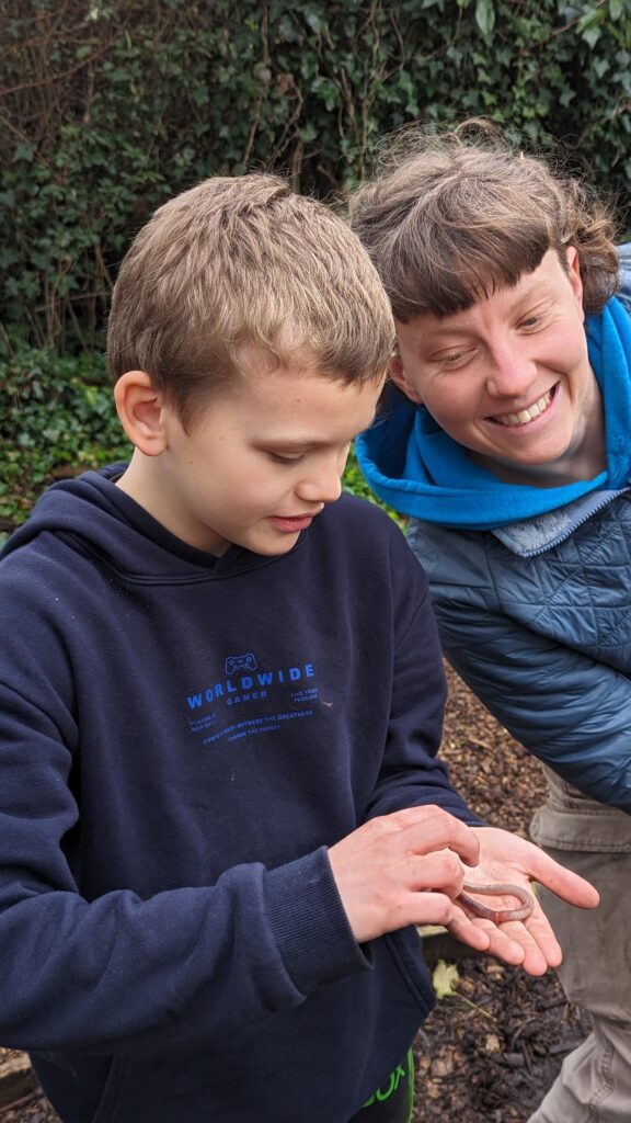ID: a Youth Options staff member smiles as they are shown a grass snake held by a young person